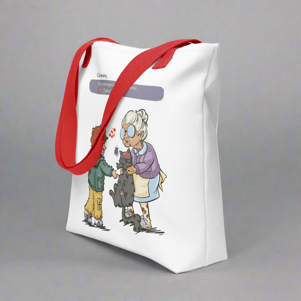 Totebag with the illustration of a granny passing a grumpy cat to her way-to-happy grand-son. The discussion goes like "It's dangerous to go alone, Take this!" referring to the Zelda game. The bag is white and has red handles.