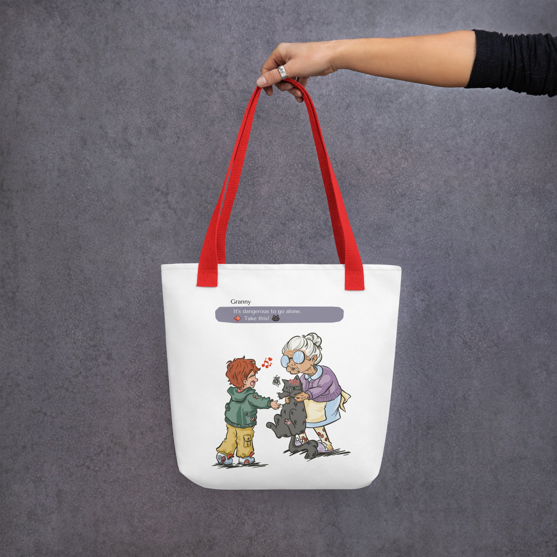 Totebag with the illustration of a granny passing a grumpy cat to her way-to-happy grand-son. The discussion goes like "It's dangerous to go alone, Take this!" referring to the Zelda game. The bag is white and has red handles.