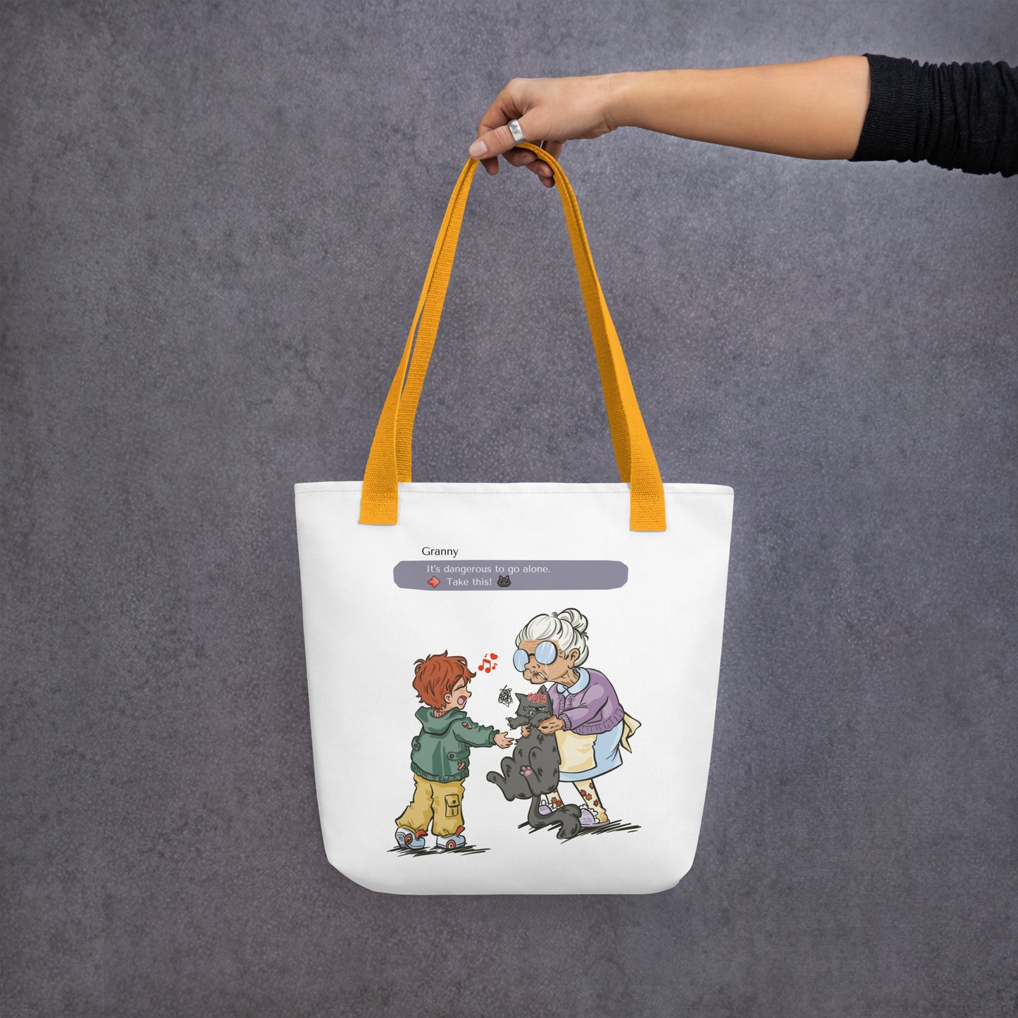 Totebag with the illustration of a granny passing a grumpy cat to her way-to-happy grand-son. The discussion goes like "It's dangerous to go alone, Take this!" referring to the Zelda game. The bag is white and has yellow handles.