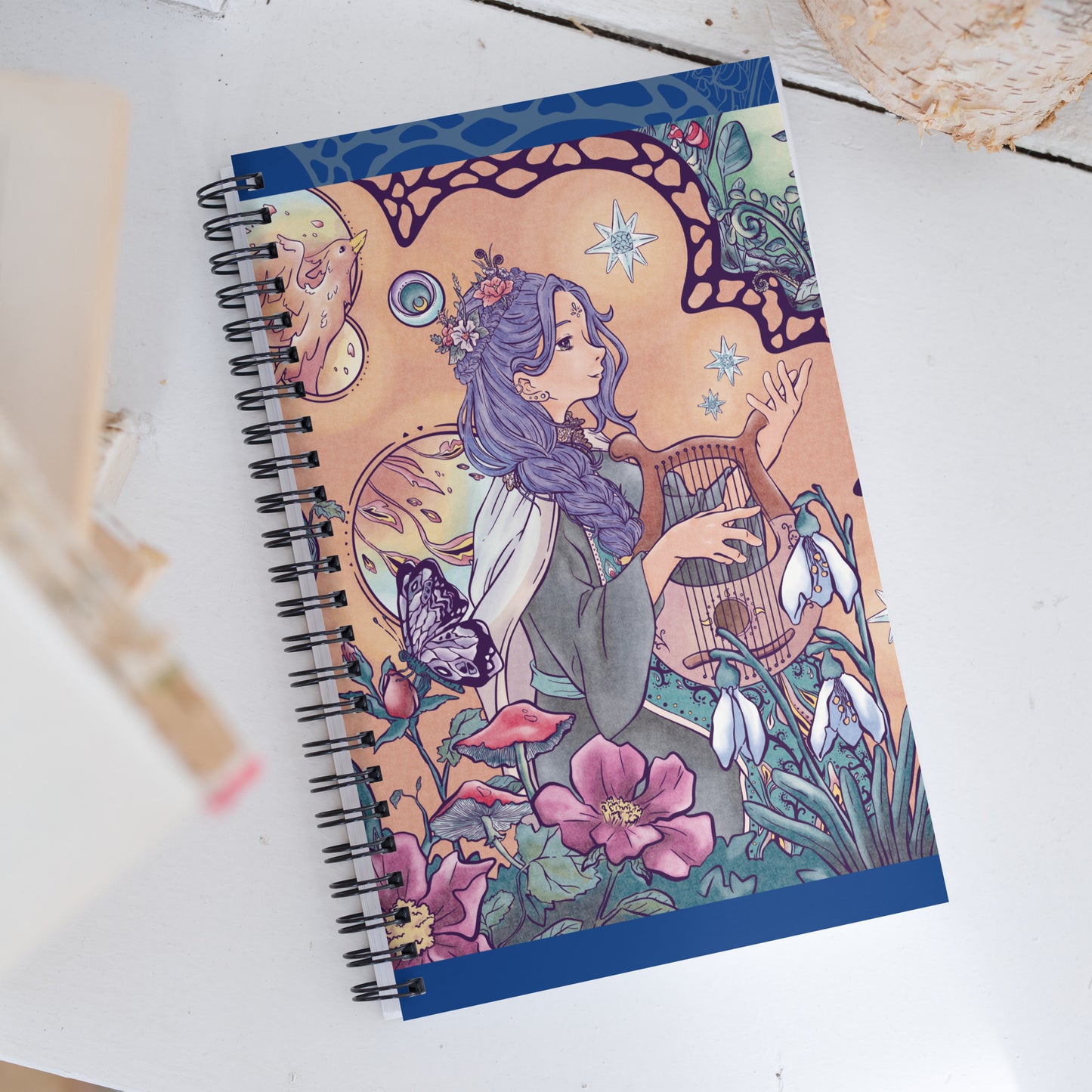 Spiral notebook with the illustration of an enchanted forest, phoenix and singing princess. The drawing is detailed and manga style. The warm color palette of the character brings a soft vibe to the green vegetation.