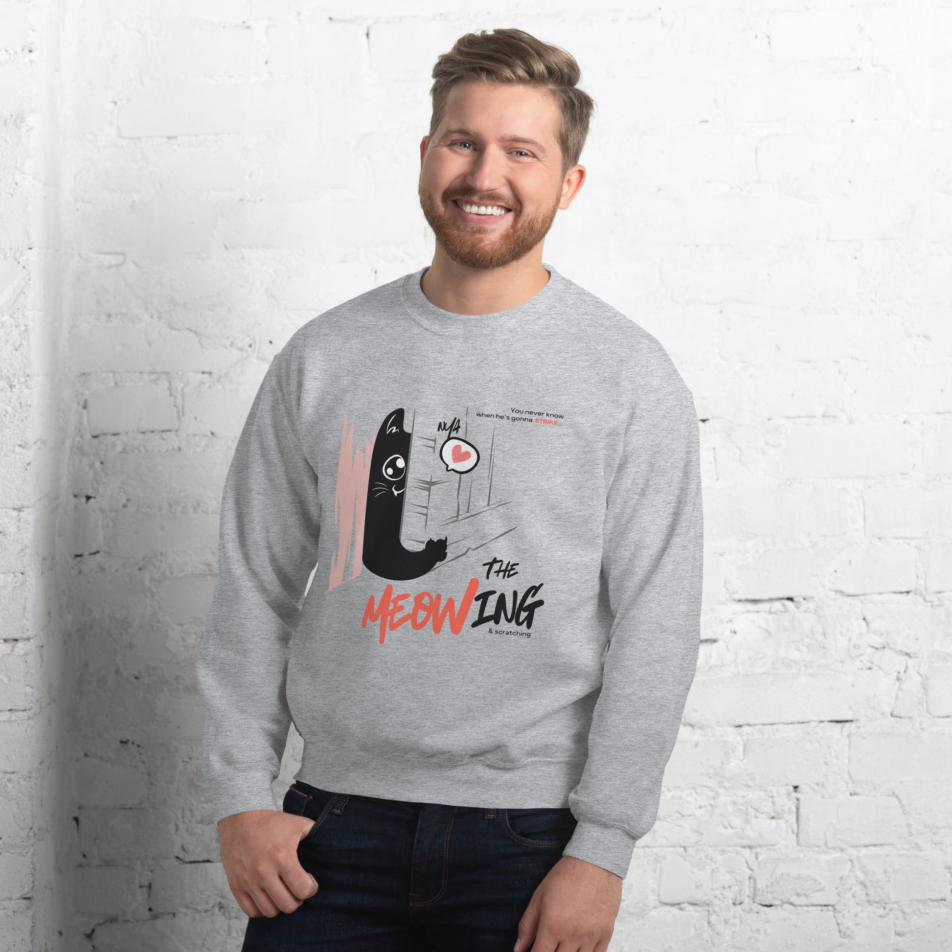 Man wearing a light grey crew neck sweatshirt with illustration of a cat trying to break into a door. Parody of the Shining, this design is called "The Meowing & scratching" because you never know when he's gonna strike. This version shows a cute cat showing the finger while trying to enter the room.